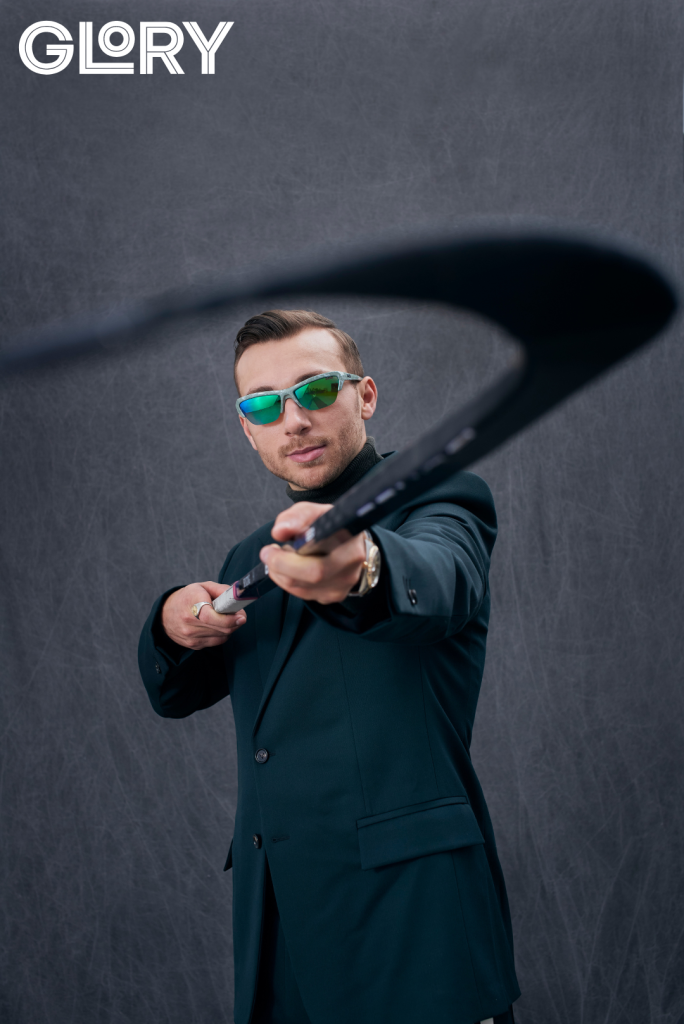 Maple Leafs forward Michael Bunting poses for a portrait with a hockey stick. Turtleneck by Louis Vuitton Watch by Rolex