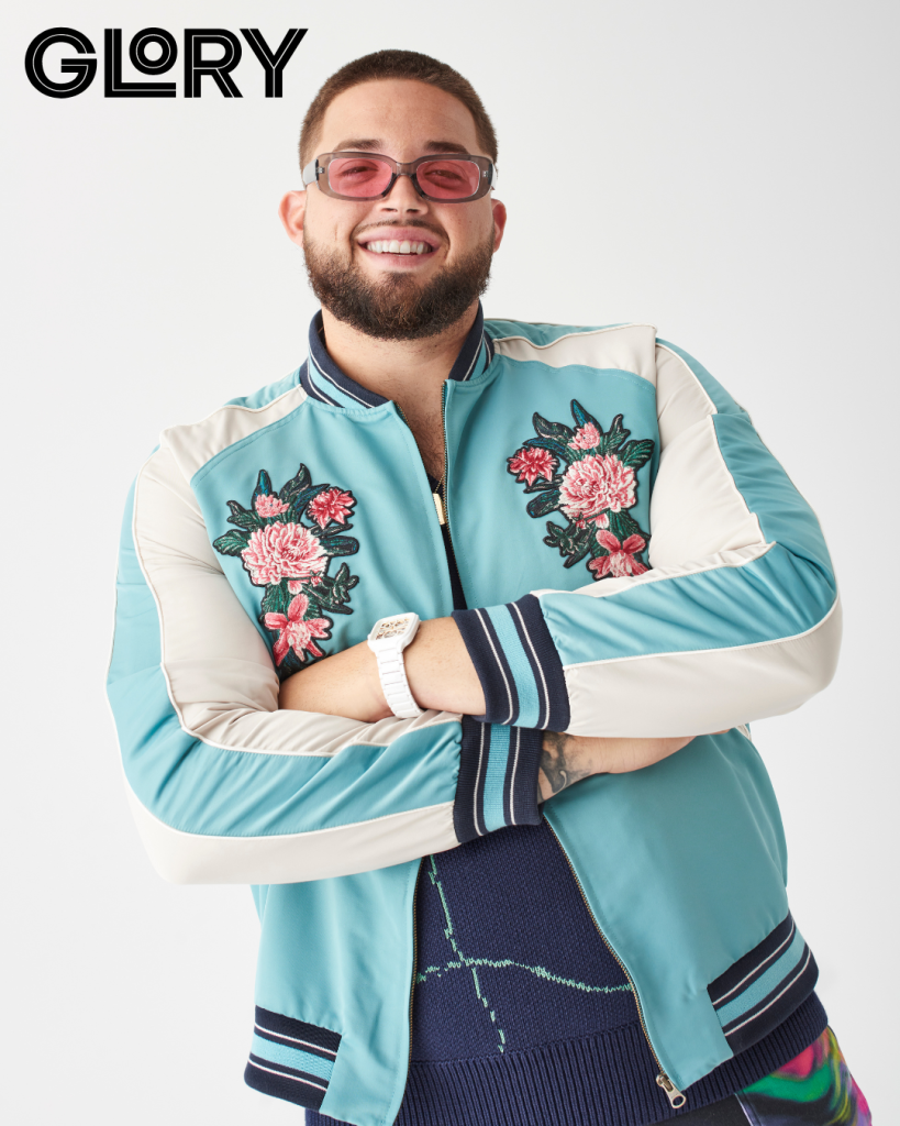 Alek Manoah smiling with pink tinted sunglasses, and a floral-embroidered silk bomber with arms crossed.