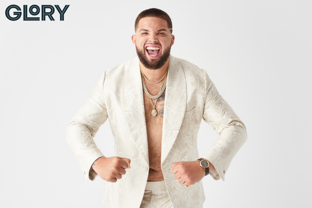 Alek Manoah wearing white jacket and chains with no shirt underneath smiling and flexing